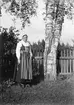 Christiane Liljefors, iklädd folkdräkt, troligen Leksandsdräkt, står vid björkar, Dalarna