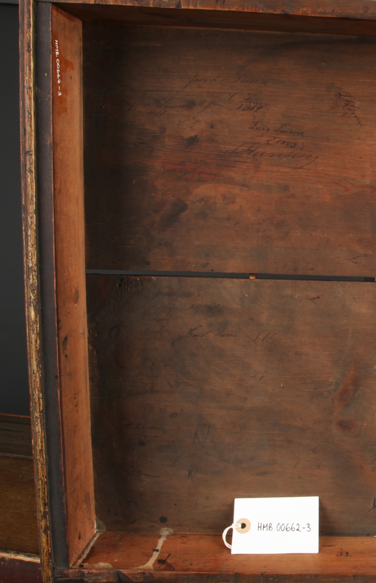 Rektangulært med skrånende skriveplate. To skuffer i front. Høye bein. Omtrent midt på beina er en hylleplate hvor det er hengslet en skapdør med en ring til håndtak. Skapdøren er hengslet i overkant og trekkes opp for å åpne.