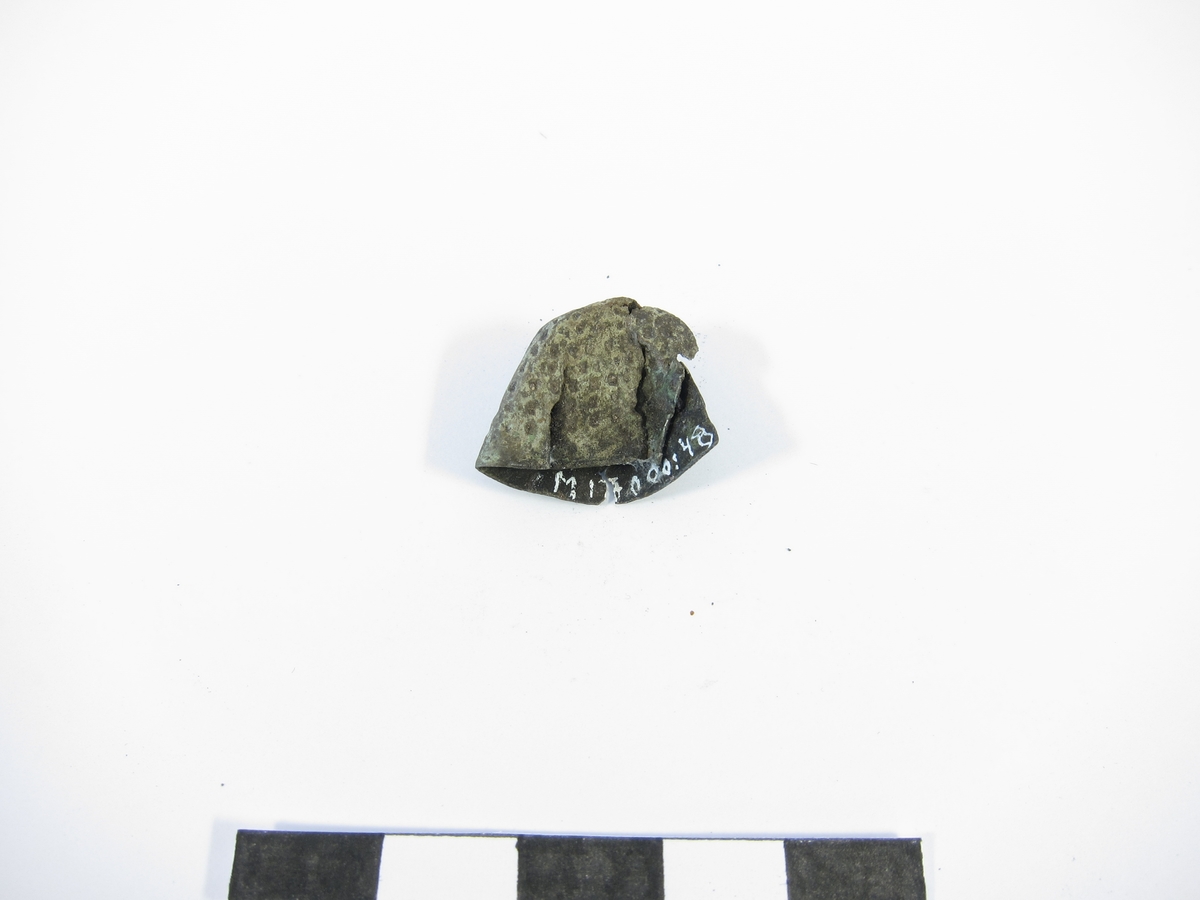 Svagt konisk fingerborg av brons med relativt glesa gropar. Nedtill är en slät rand med fabriksstämpel: H intryckt (se bild).