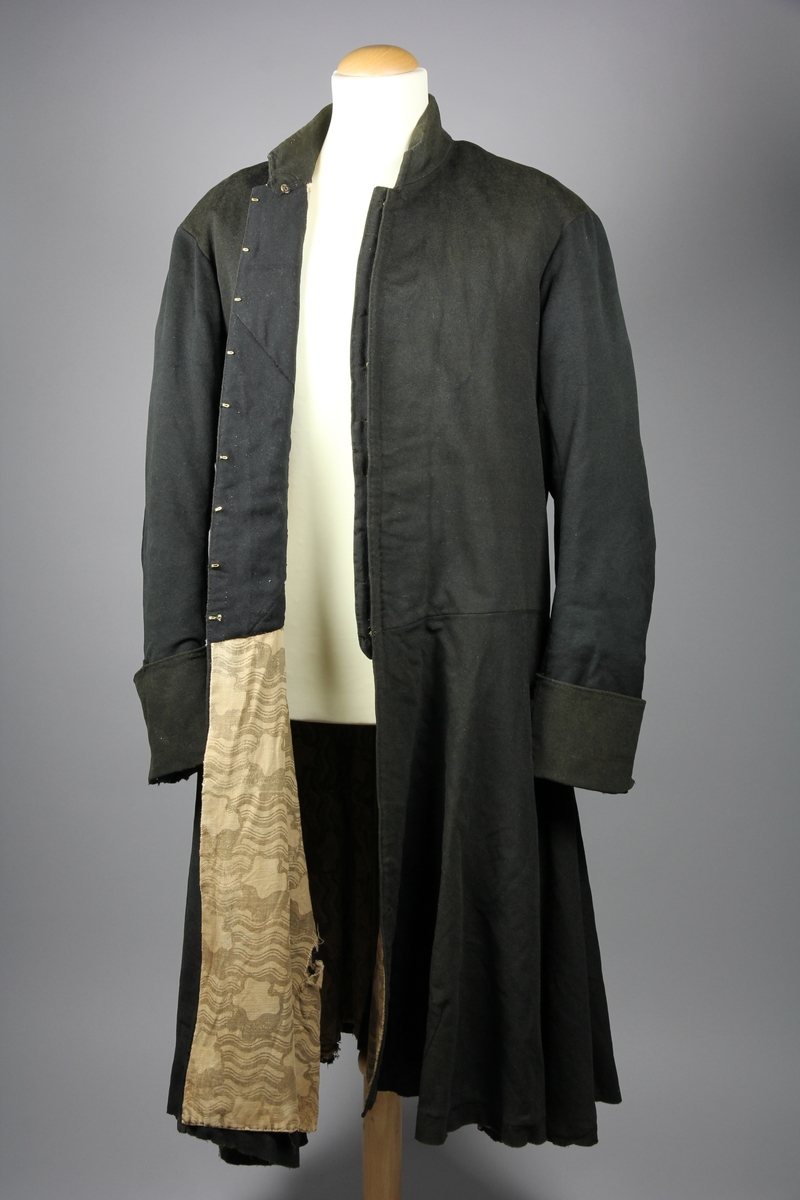 Rock av svart tuskaftsvävt yllekläde. Rocken har en 3,5 cm hög ståkrage. Ärmarna har två längsgående sömmar och 11 cm breda uppslag. Ryggstycket är sammanfogat av fyra våder. Vid axlarna är en trekantig kil infälld på var sida. Troligen en besparing. I höfthöjd har rocken en mittsöm som löper hela vägen runt. Skörten är skurna med stort omfång och rundade. I mitten bak är båda skörten förlängda med en remsa som överlappar på höger sida i ett sprund. Nederkanten har på flera ställen infälda stycken, troligen för att utnyttja tyget maximalt eller som lagningar. Rocken stängs fram med 9 par hyskor och hakar av grov mässingstråd.

Fodret är sytt av minst tre olika tyger. Överst ett grövre grårandigt linnetyg med två infällda innerfickor. Ärmarna är fodrade med oblekt linne och har vaddering av bomullsvadd. Nederst i båda ärmsluten finns rester av blåfärgade linneremsor. Kanske ett tidigare fodertyg eller ett mellanlägg. Rockens nedre foderdel är av ett tunt linne eller bomullstyg med tryckt mönster i brunt på ljusbrun botten. Möjligen är den övre delen av fodret yngre än den nedre. Slitaget på den övre är mindre än på de nedre. Hela rocken är handsydd, men det förekommer lagningar och bättringar med raksöm från symaskin. Det finns flera mindre och några större hål samt sömmar som släppt.