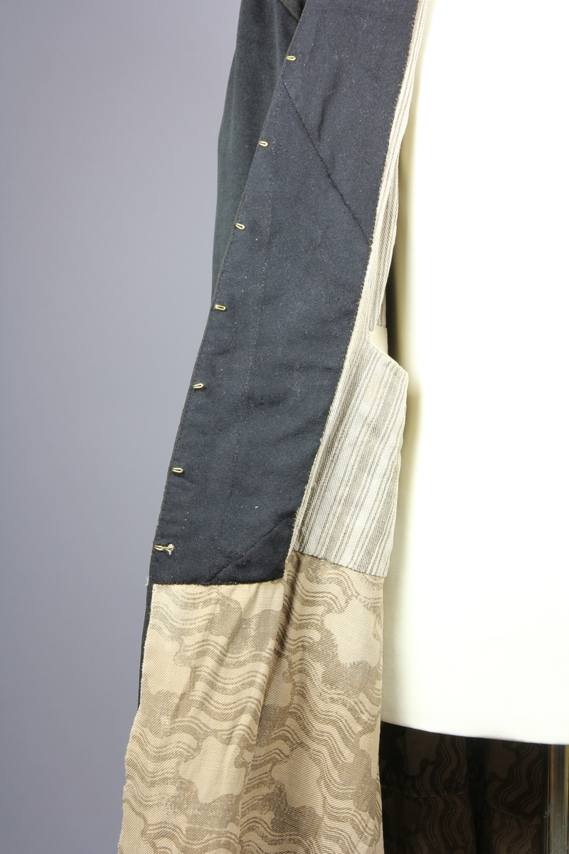 Rock av svart tuskaftsvävt yllekläde. Rocken har en 3,5 cm hög ståkrage. Ärmarna har två längsgående sömmar och 11 cm breda uppslag. Ryggstycket är sammanfogat av fyra våder. Vid axlarna är en trekantig kil infälld på var sida. Troligen en besparing. I höfthöjd har rocken en mittsöm som löper hela vägen runt. Skörten är skurna med stort omfång och rundade. I mitten bak är båda skörten förlängda med en remsa som överlappar på höger sida i ett sprund. Nederkanten har på flera ställen infälda stycken, troligen för att utnyttja tyget maximalt eller som lagningar. Rocken stängs fram med 9 par hyskor och hakar av grov mässingstråd.

Fodret är sytt av minst tre olika tyger. Överst ett grövre grårandigt linnetyg med två infällda innerfickor. Ärmarna är fodrade med oblekt linne och har vaddering av bomullsvadd. Nederst i båda ärmsluten finns rester av blåfärgade linneremsor. Kanske ett tidigare fodertyg eller ett mellanlägg. Rockens nedre foderdel är av ett tunt linne eller bomullstyg med tryckt mönster i brunt på ljusbrun botten. Möjligen är den övre delen av fodret yngre än den nedre. Slitaget på den övre är mindre än på de nedre. Hela rocken är handsydd, men det förekommer lagningar och bättringar med raksöm från symaskin. Det finns flera mindre och några större hål samt sömmar som släppt.