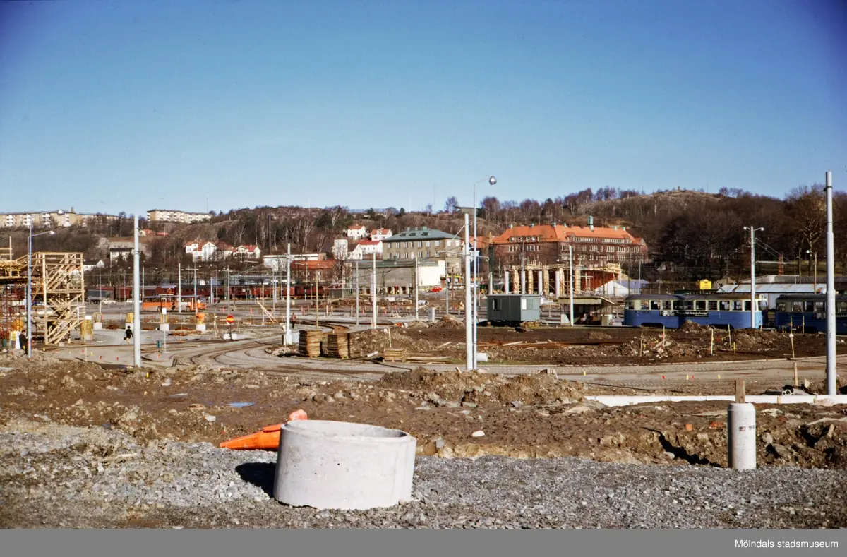 Vy från Broslättsgatan över spårvägslinjen 4:ans vändslinga mot byggnationen av den nya Mölndals Bro, ca 1974-1975. I fonden uppe på höjden till vänster ses bostadsbebyggelse i stadsdelen Enerbacken. I mitten ses huset Kvarnbygatan 1, numera Nämndemansgatan 1 samt Kvarnbyskolan.