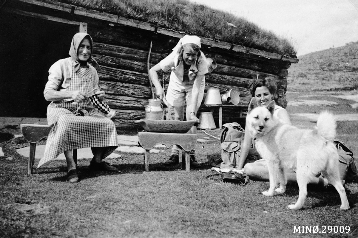 På Bakka-setra (Gravmobakken). Marit Erlandsdatter Bakken (1876-1954) med bundingen (rutahosser). To bydamer er med og rører mussmøret kaldt. 