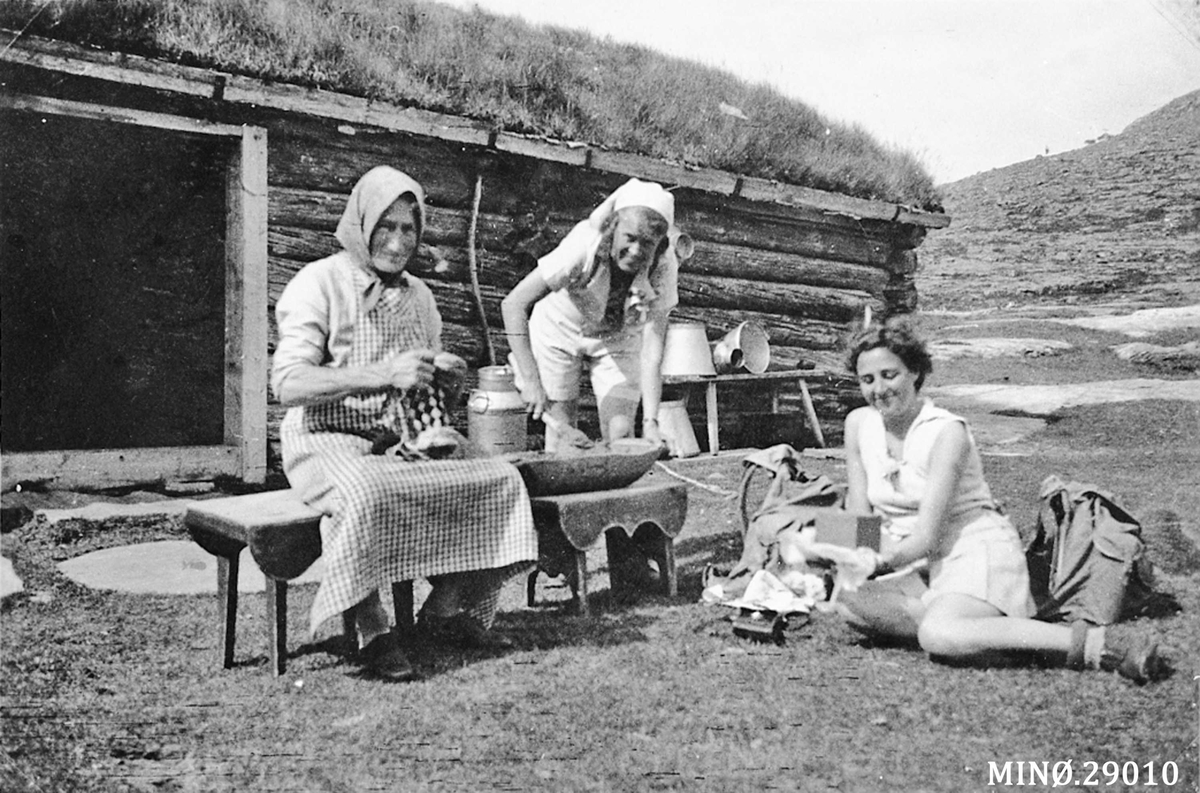 På Bakka-setra (Gravmobakken). Marit Ellandsdatter Bakken (1876-1954) med bundingen (rutahosser). To bydamer er med og rører mussmøret kaldt. 