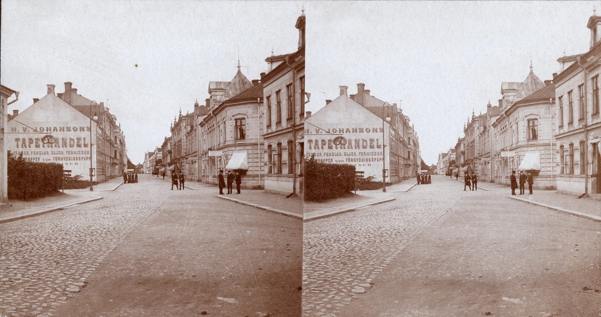 Stereobild. Stadsmotiv. Tapethandel, bageri. Östra Långgatan i Köping.