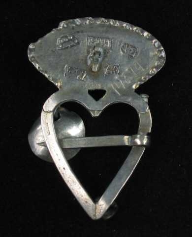 Hjertesprette av sølv med oval krone loddet til hjertet. Krona har tråddekor: fire trådspiraler lagt i s-form, stilt sammen parvis. Mellom disse er det en innfattet rubinrød fasettslipt glassperle (eller stein?) Dette feltet er begrenset av to trådbånd, det innerste av glatt tråd og det ytterste av tvinnetråd. Det er opprinnelig festet tre skåleløv til hjertegrinda, to mangler. Tornen er glatt og er festet på tvers av grinda. Flere stempler på baksida.
