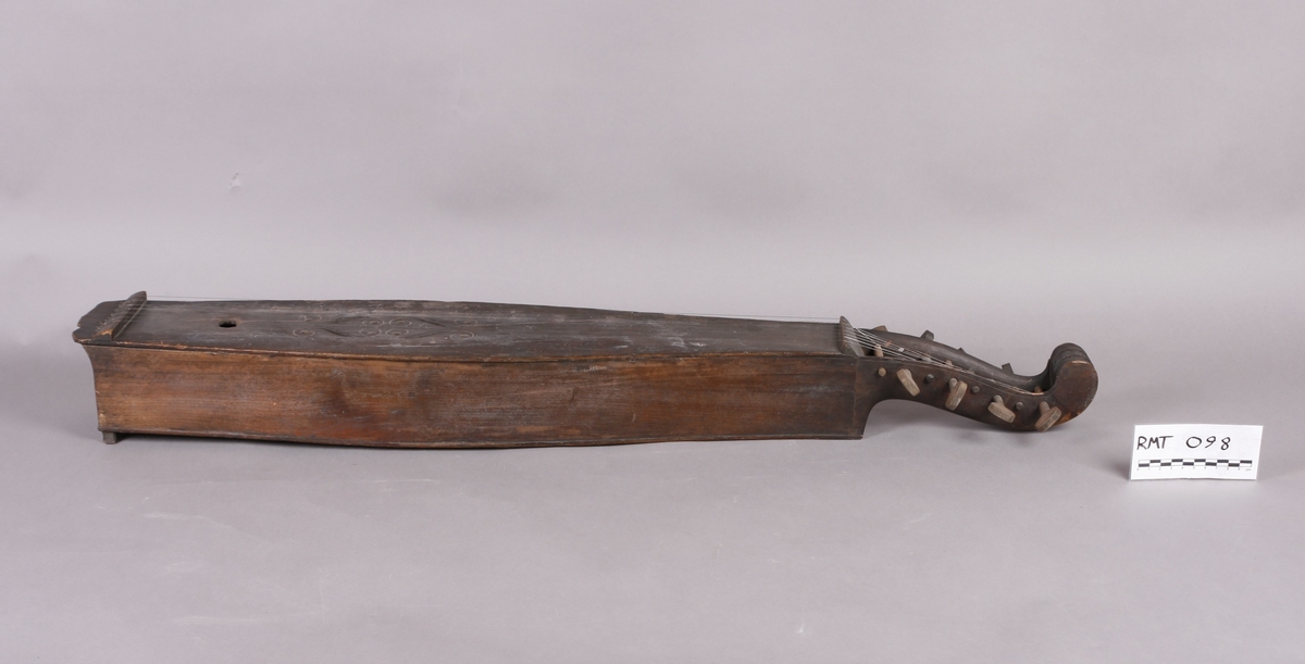 Korpus sammensatt av 4 bord, bunn og lokk limt på sidene. Lokk og bunnn i nåltre, sarger i løvtre. Hode og skruekasse i ett stykke - av løvtre. Hode i form av enkel snekke, 8 stemmeskruer. Sidene buket (Valdrestype), øvre fot mangler. 3 lydhull: 1 mindre grovt ovalt ved anslag (ant. etter kvist, (JV)), samt to par s-formet hull parvis speilvent (lager en hjerteform!).
Strengene festet i stifter like bak stol. Høyre sadel og forstykke festet til korpus med trenagler. Hele instrumentet er beiset mørk brunt. Skala på melodistrengen. Alle noter og pyramider mangler. Spor i lokket etter notene, ca 16 stk. Spor etter to strengeleder - gir korteste strenge ytterst.