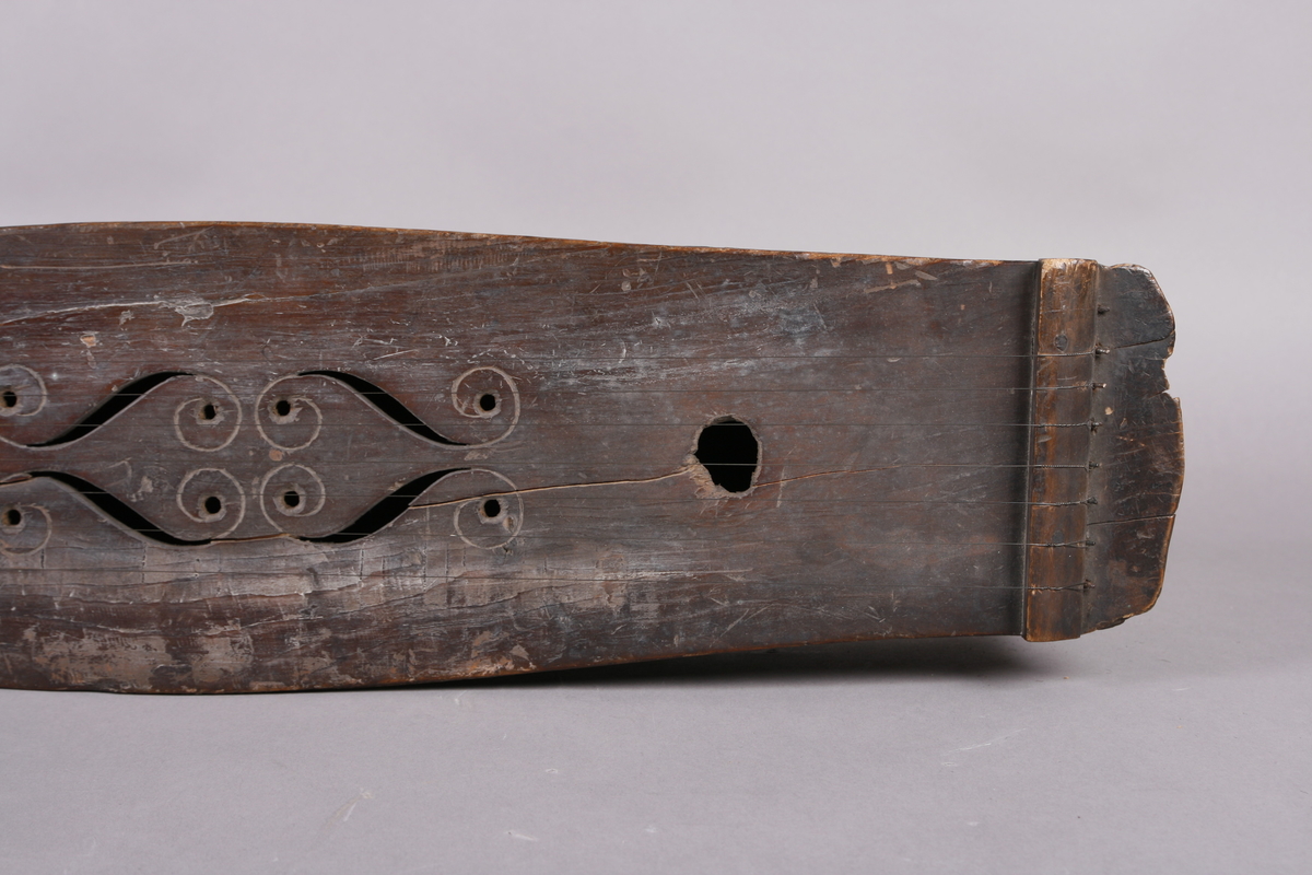 Korpus sammensatt av 4 bord, bunn og lokk limt på sidene. Lokk og bunnn i nåltre, sarger i løvtre. Hode og skruekasse i ett stykke - av løvtre. Hode i form av enkel snekke, 8 stemmeskruer. Sidene buket (Valdrestype), øvre fot mangler. 3 lydhull: 1 mindre grovt ovalt ved anslag (ant. etter kvist, (JV)), samt to par s-formet hull parvis speilvent (lager en hjerteform!).
Strengene festet i stifter like bak stol. Høyre sadel og forstykke festet til korpus med trenagler. Hele instrumentet er beiset mørk brunt. Skala på melodistrengen. Alle noter og pyramider mangler. Spor i lokket etter notene, ca 16 stk. Spor etter to strengeleder - gir korteste strenge ytterst.