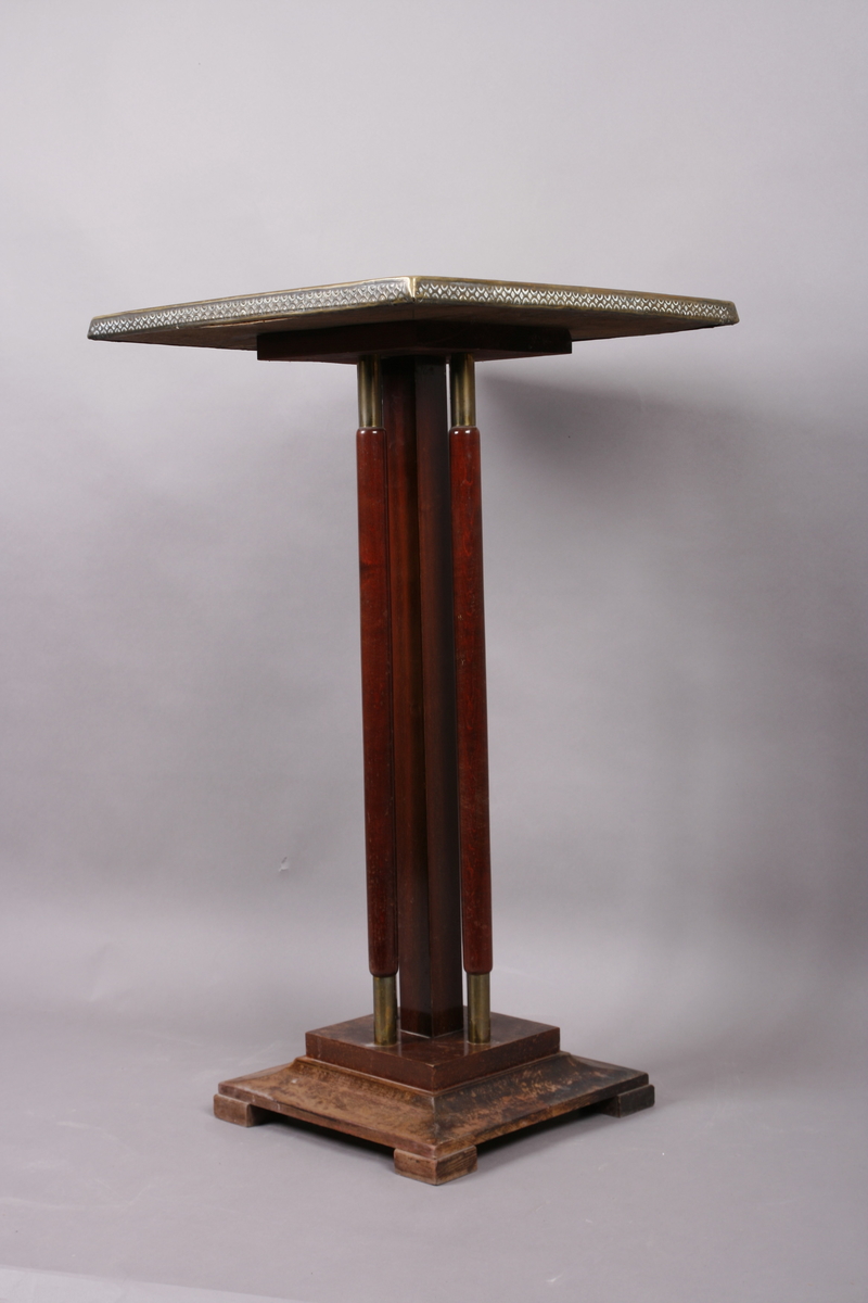 Firkantet med fire søyleben. Bordplate i messing med preget dekor.