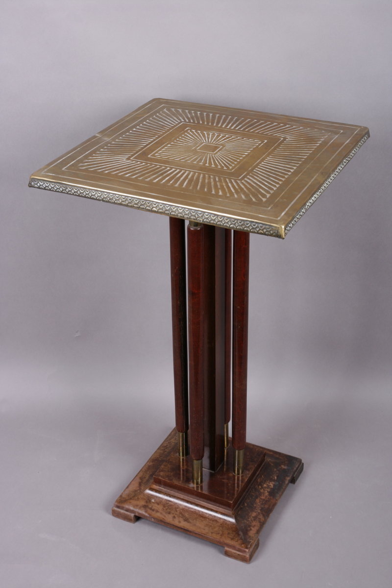 Firkantet med fire søyleben. Bordplate i messing med preget dekor.