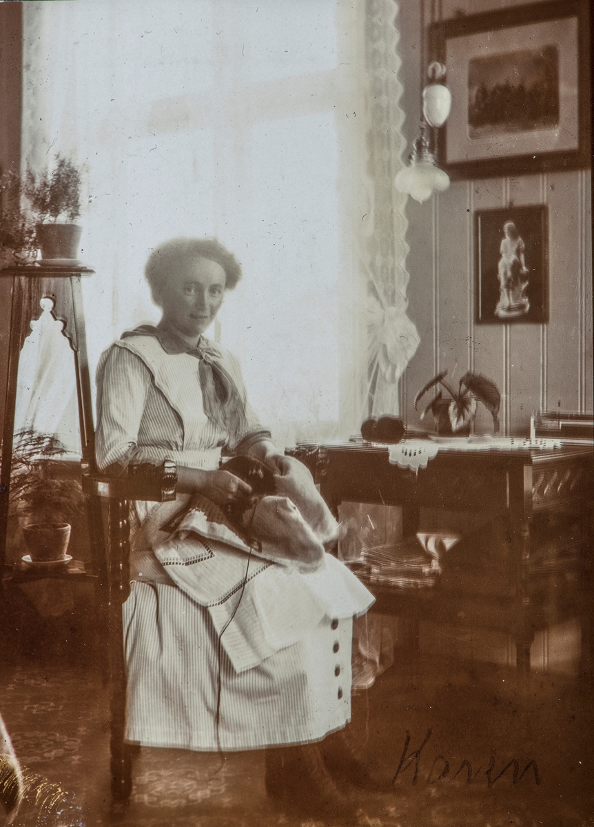 Interiør, kvinne med håndarbeid i fanget, sittende. (Benningstad eller ingeniørboligen?)