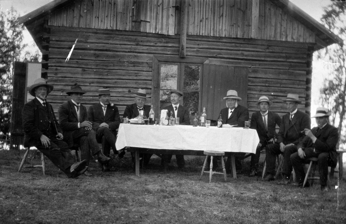 Herreselskap, dekket bord, utendørs. Gruppe menn sittende, dress og hatt.