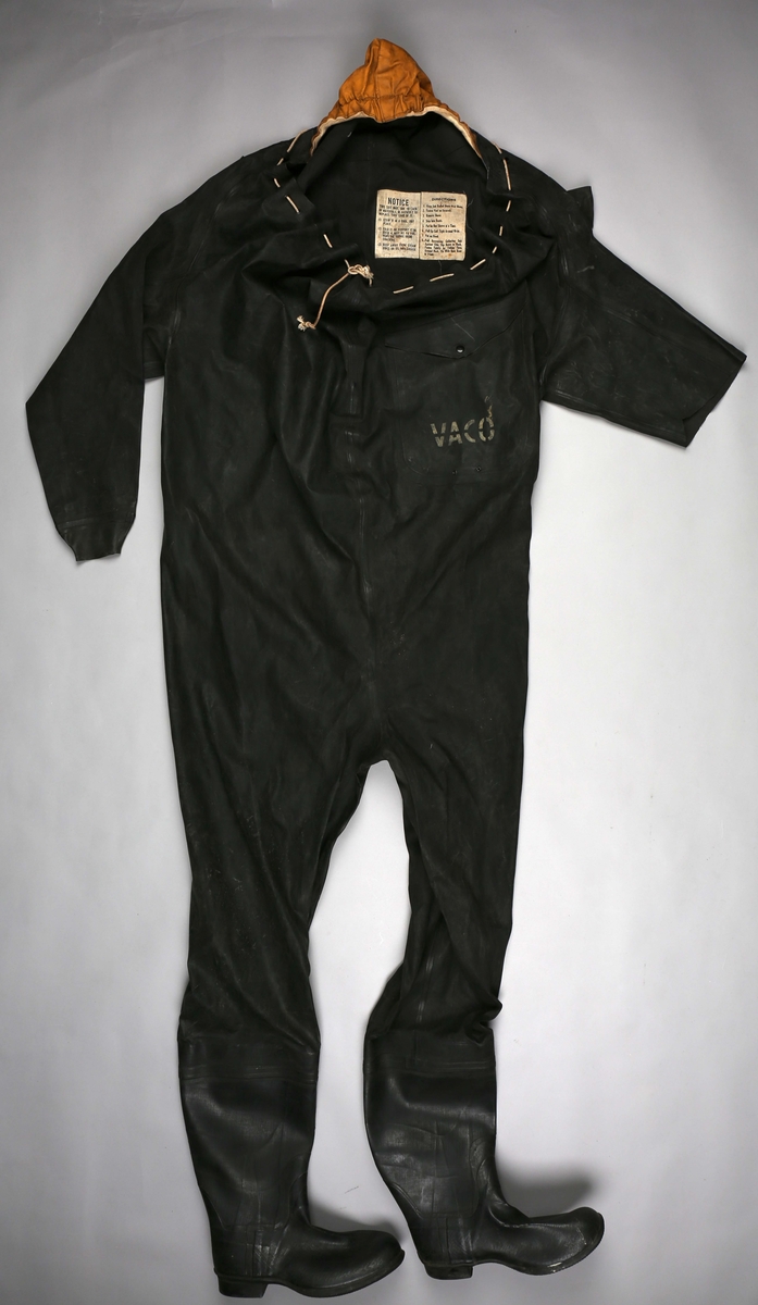 Redningsdrakt med hette. Hel overlevelsesdrakt med lomme i front og integrerte støvler. Drakten har ingen åpning i front men den er så stor rundt halsen at den kan draes opp over mage og armer. Snøres sammen ved hjelp av tau. Høyre arm mangler/er klippet av.