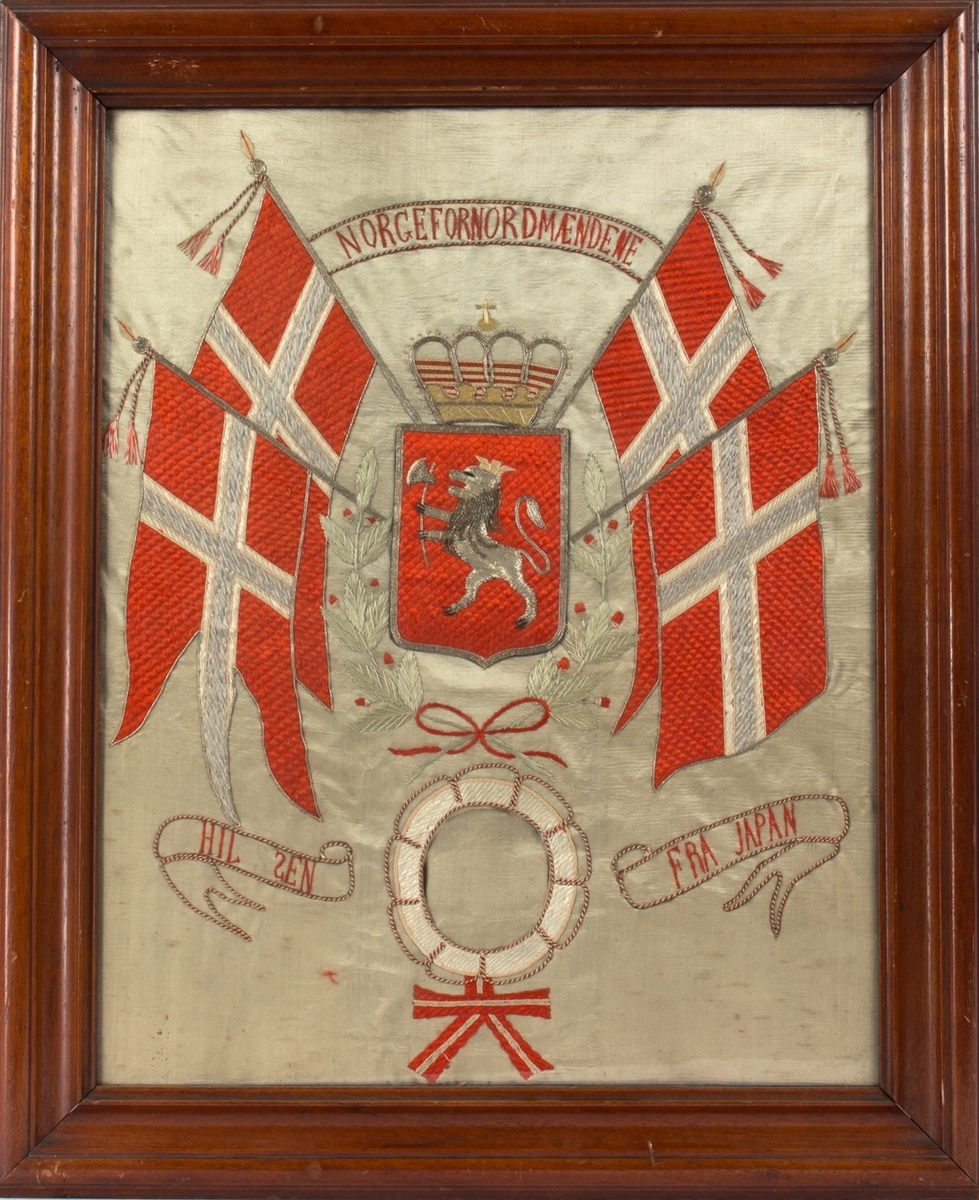 Brodert silkebilde med tekst NORGE FOR NORDMÆNDENE. Midt i motivet norsk riksvåpen med krone omkranset av to norske flagg på hver side. Under brodert livbøye med plass til fotografi/portrett uten at det har vært montert noe bilde.