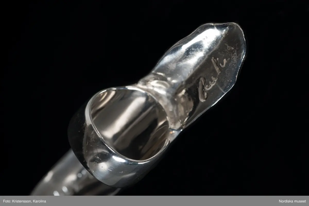 Ring av silver, överdel i form av avlång avgjutning av fingerrygg. Underdel bestående bred ring med slits på ena sidan. Undertill graverad "Cornelia".
/Leif Wallin 2018-02-09