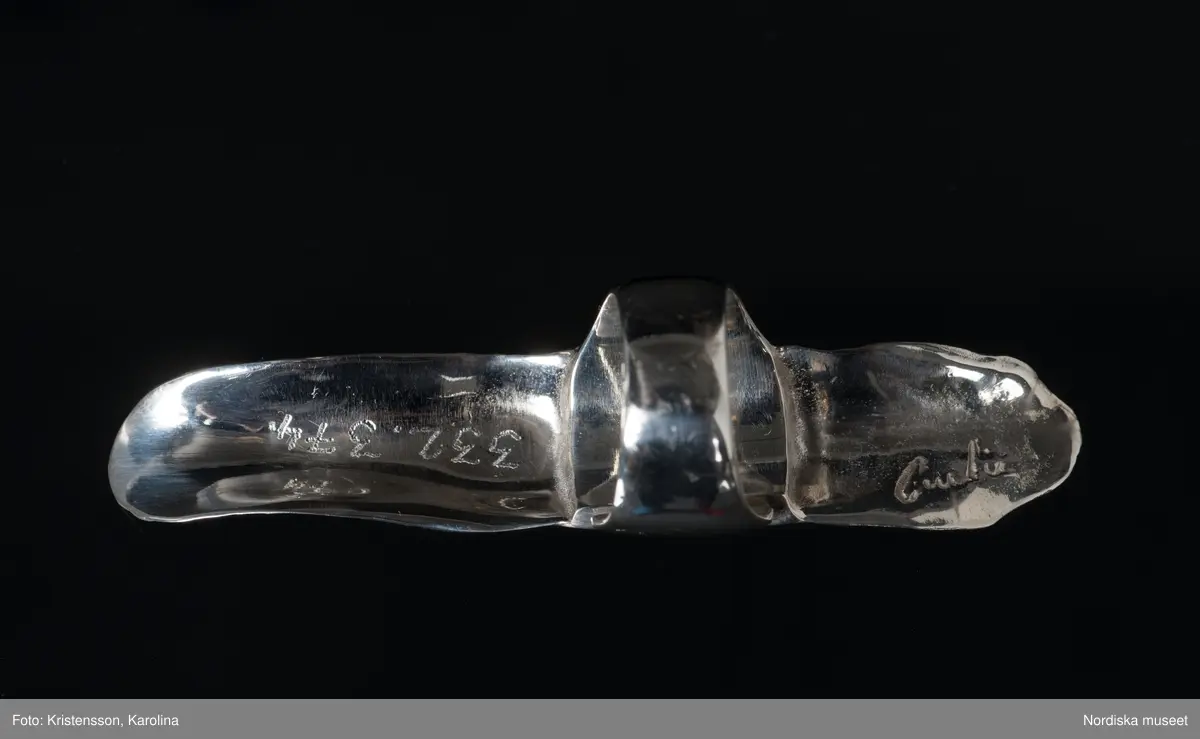 Ring av silver, överdel i form av avlång avgjutning av fingerrygg. Underdel bestående bred ring med slits på ena sidan. Undertill graverad "Cornelia".
/Leif Wallin 2018-02-09