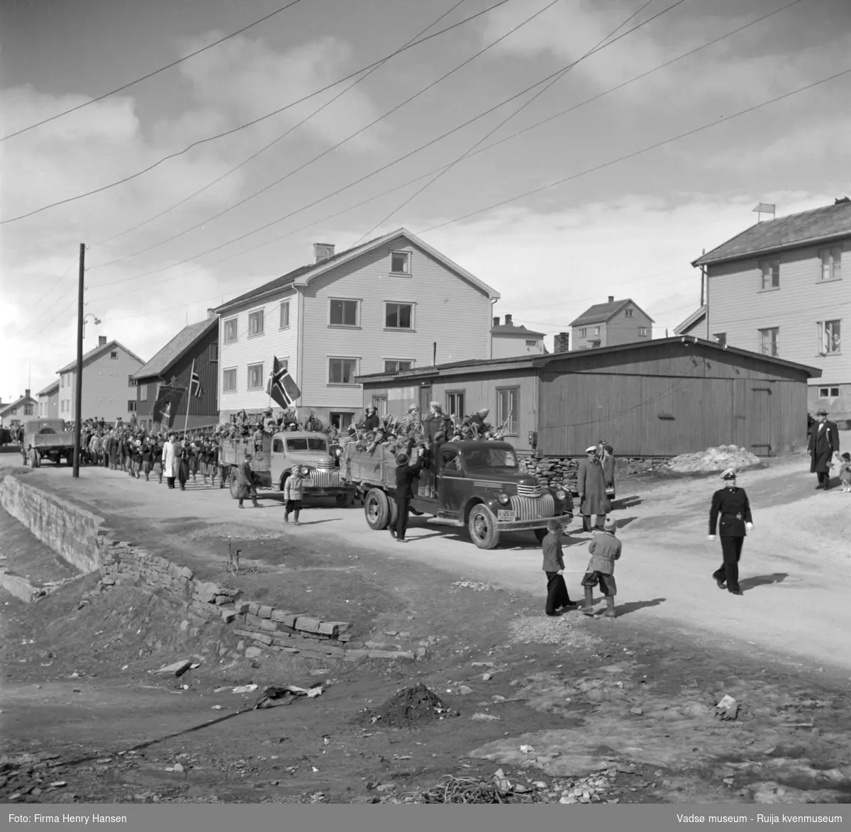 Vadsø 17 mai 1952. Folketog på vei østover i Havnegata. To lastebiler med jublende barn med flagg, den nærmeste bilen har nummerskilt Y-2536 og den bakerste antakeligvis Y-2519. En trehjulssykkel i forkant av bildet.
Begge lastebilene er Chevrolet årsmodell 1946-47. Y-2536 var registrert på Halfdan Kristoffersen