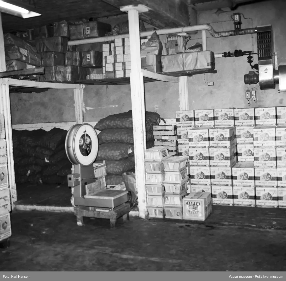 Nord-Norges salgslag Vadsø, 1964. Grønnsaklageret med  bl.a fruktkasser, grønnsakskasser og potetsekker.