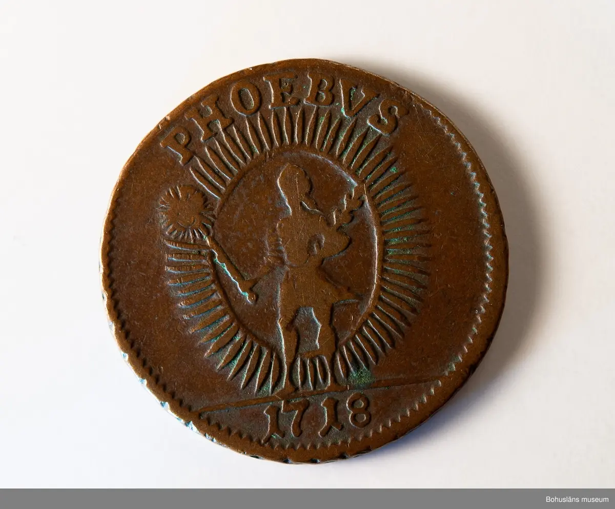 1 daler silvermynt 1718, "PHOEBVS", koppar, Stockholm.
Mynt präglat under Karl XII:s regeringstid.

Åtsidan: 
Frånsidan: I DALER S.M. på tre rader.
Myntets ytterrand refflad, vinkelrätt.

Material: koppar med tvångsvärde 1 daler silvermynt.

Karl XII 1682 - 1718, kung av Sverige 1697-1718.
Förvärvsdatum okänt.