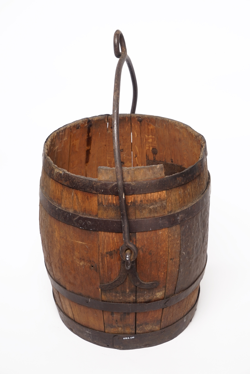 Tretønne med hank av metall, forsynt utvendig med fire metallringer. Delvis belagt med metallbelegg inn og utvendig for antatt reparasjon av tønnen.