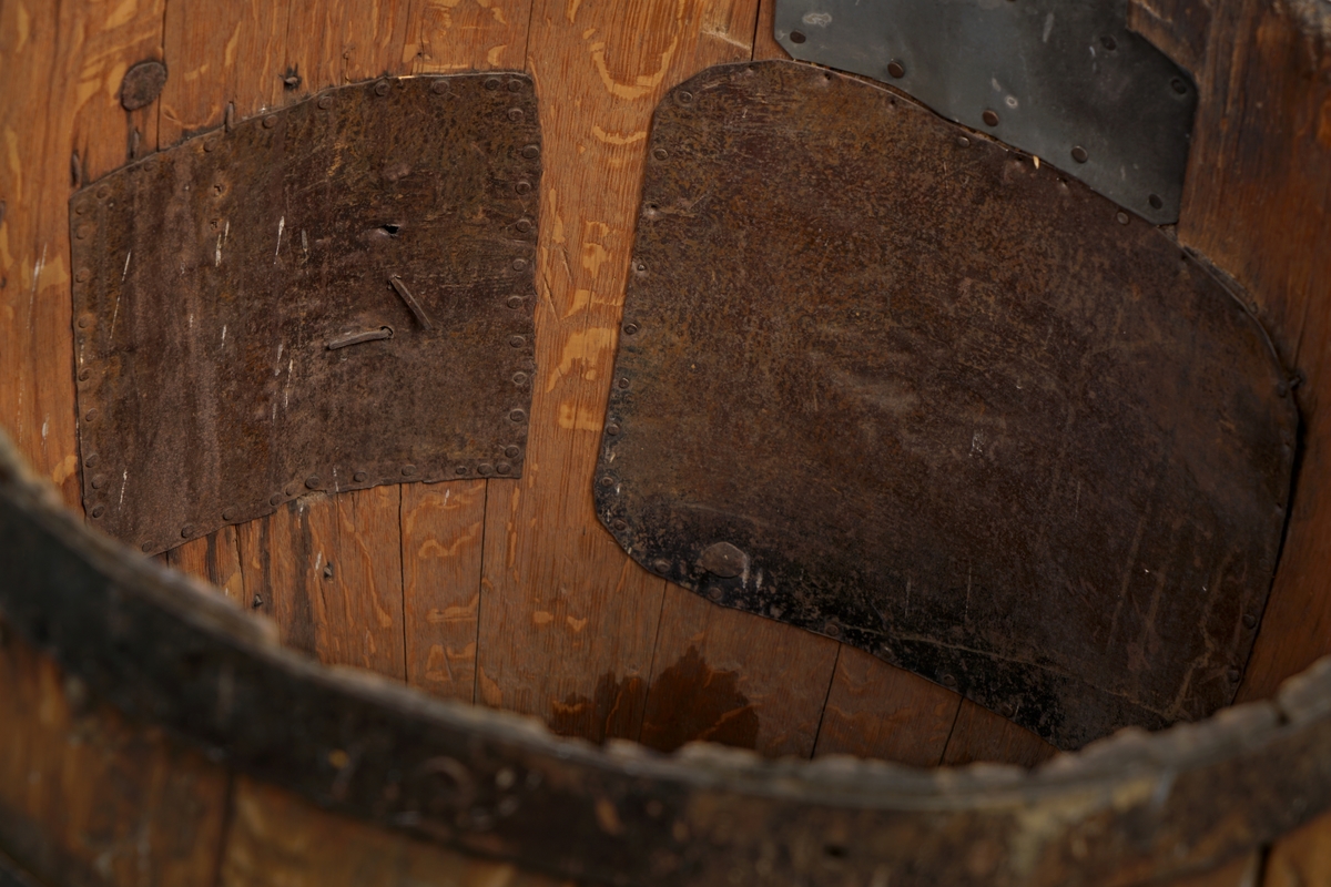 Tretønne med hank av metall, forsynt utvendig med fire metallringer. Delvis belagt med metallbelegg inn og utvendig for antatt reparasjon av tønnen.