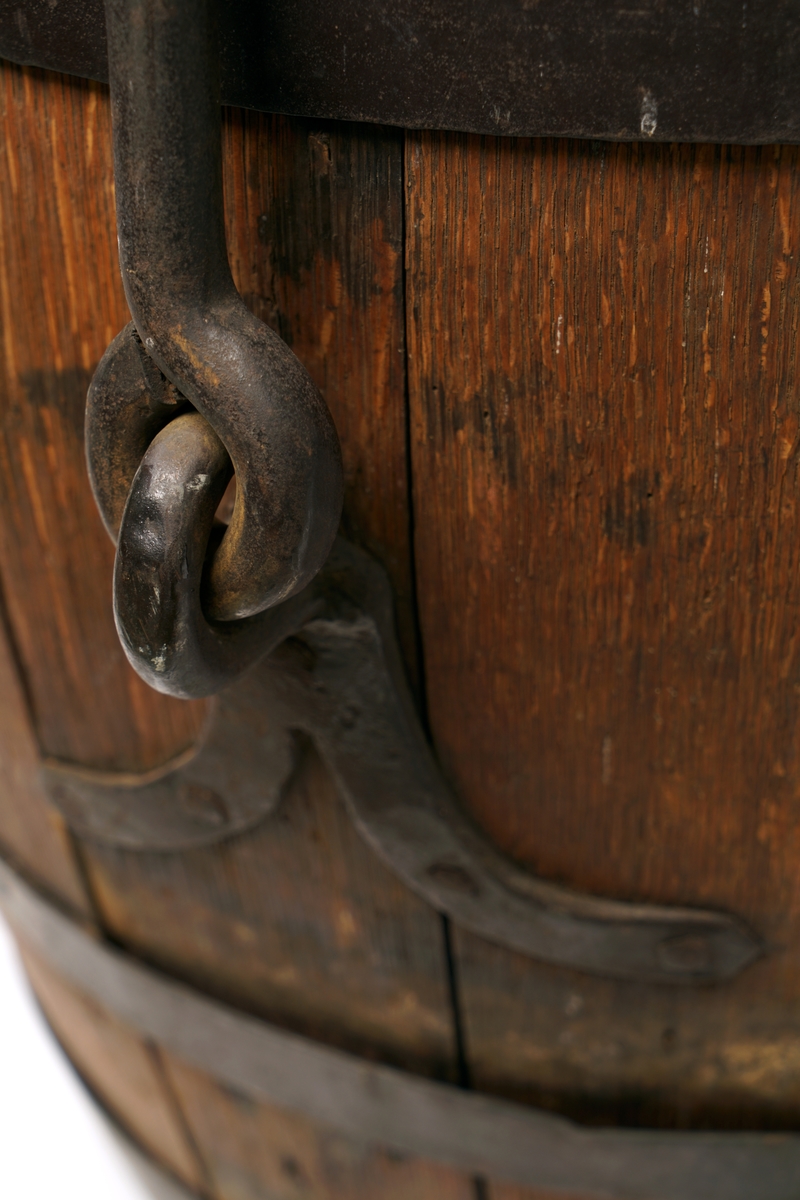 Tretønne med hank av metall, forsynt utvendig med fire metallringer. Delvis belagt med metallbelegg inn og utvendig for antatt reparasjon av tønnen.