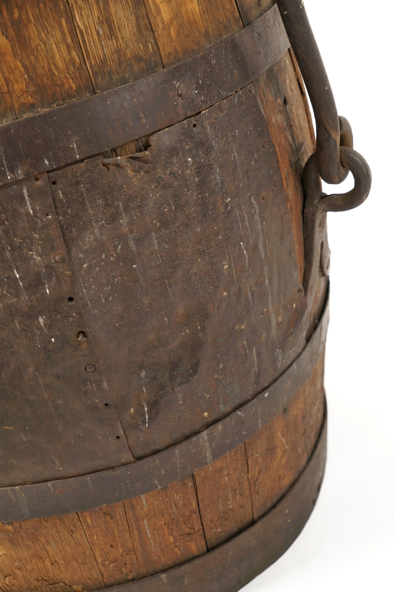 Tretønne med hank av metall, forsynt utvendig med fire metallringer. Delvis belagt med metallbelegg inn og utvendig for antatt reparasjon av tønnen.