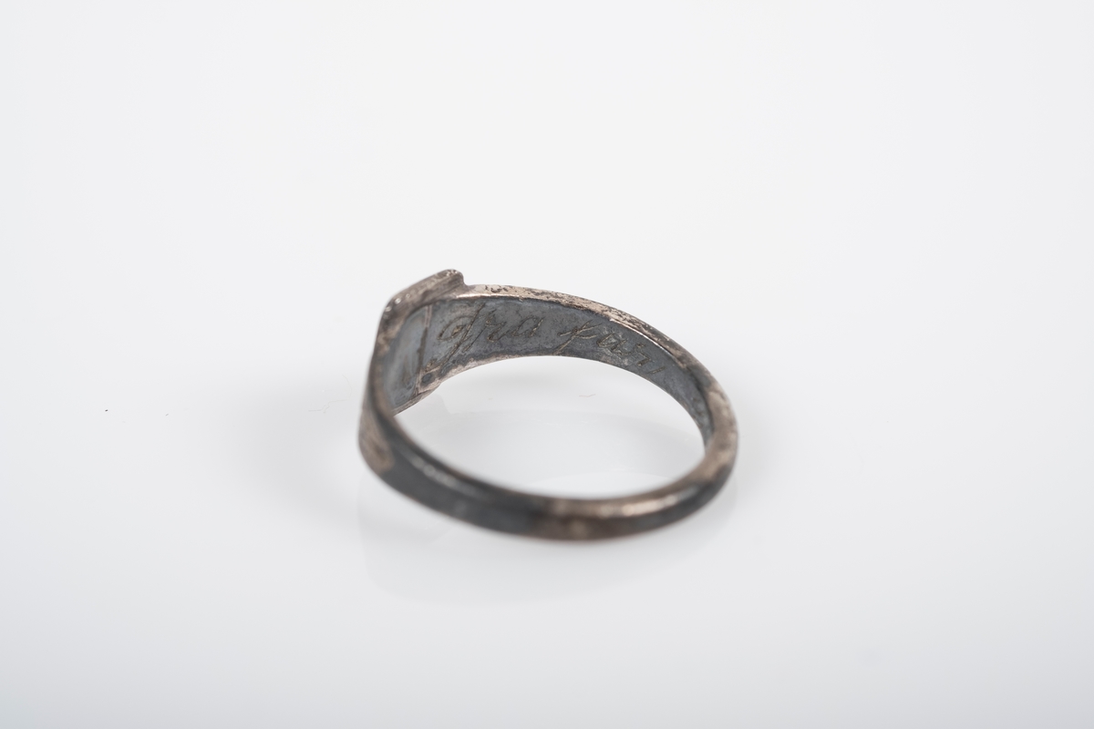 Liten rund ring med et firkantet monogram foran med initialene BL inngravert. På innsiden er det inngravert "Fra Far Grini 1942-43".