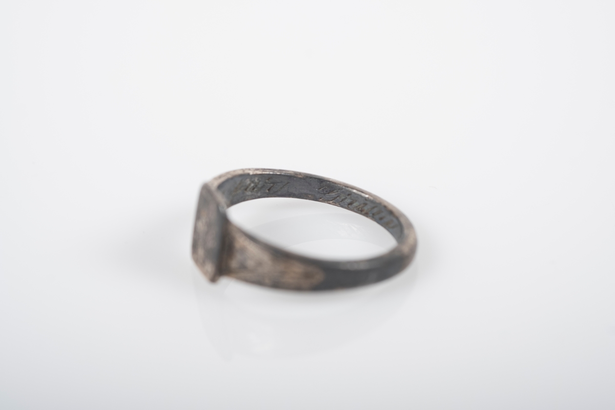 Liten rund ring med et firkantet monogram foran med initialene BL inngravert. På innsiden er det inngravert "Fra Far Grini 1942-43".