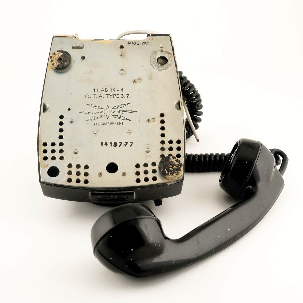 Telefonapparat med dreie/tallskive nummerert fra 0 til 9 som er snudd opp/ned. Telefonrør  er tilkoblet med spiralisert ledning. Det er tilkoblet ledning som er avkuttet , ment for tilkobling til vegguttak. Under/til venstre for dreieskiven er det montert en trykknapp. Uvisst hvilken funksjon denne har. På undersiden er det festet to gummi knotter/ben hvorav to er borte.