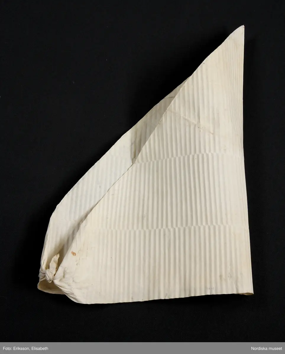 Huvudliggaren:
"a-r Kvinnodräkt. a. kjol, b. förkläde, c. kappa, d. tröja, e. överdel
f.1 - f.4 huvudbonad, (4 delar), g. bälte, h. kjolsäck, i. handskar, j: silkesduk, k. bokkläde, l. psalmbok, m.1- m.2 Bältehängen med silversked och skedpåse, n. nåletui, o.1 kniv, o.2 gaffel, o.3 slida av saffian, p. lit. påse, q. kedjekniv, r. ring.  Ink. 13/7 1903 [från] Eriksson, Erik, herr, Kåsta, Vingåker jämte 95.162 [...]. [Brukningsort:] Södermanland Oppunda hd Vingåker sn."

b. Högtidsförkläde längd 96 cm, vådbredd 80 cm. Av grön rask, nedtill kant och skoning av svart kläde, upptill 3 cm bred linning av svart kläde. Nederkanten broderad med en vågrad i kedjesöm med gult silke, ovanför denna en staket-och 6 stjälksömsrader i omväxlande gult och rosa silke samt e rader band av ylle och silke i lila, rött o gult. Linningen broderad med tre rader flätsöm i lila och gult. På sidor om linningen 6 cm fria ändar. Knytband av mönstrat bomullsband.

f: 1-4 Huvudbonad "Huckel"
f:1 Sydd stomme av halmflätor med stödande träpinne i kullen.
f:2 Fyrkantigt tygstycke av bomullslärft, svept kring stommen.
f:3 Mössa av rött kläde broderat med gult, brunt och grönt silke i tambursöm.
f:4 Kvadratiskt kläde av vit bomullslärft, vikt i tresnibb, stärkt och goffrerat

g. Bälte, längd 69 cm utan spänne, bredd 7,5 cm.
Av styvt skinn överklätt med rött ylletyg och besatt med 14 kupiga silverbucklor med punsad dekor, kraftigt spänne av samma typ med hake och ögla. På spännet flera stämplar bl.a 3 kronor, I P samt C.
/Berit Eldvik 2007-02-20