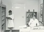 Interiör. Företagshälsovården (FHC). Margit Henocksson, sjuksköterska ? Gula kontoret.
Personer: Margit Henocksson? och okänd
