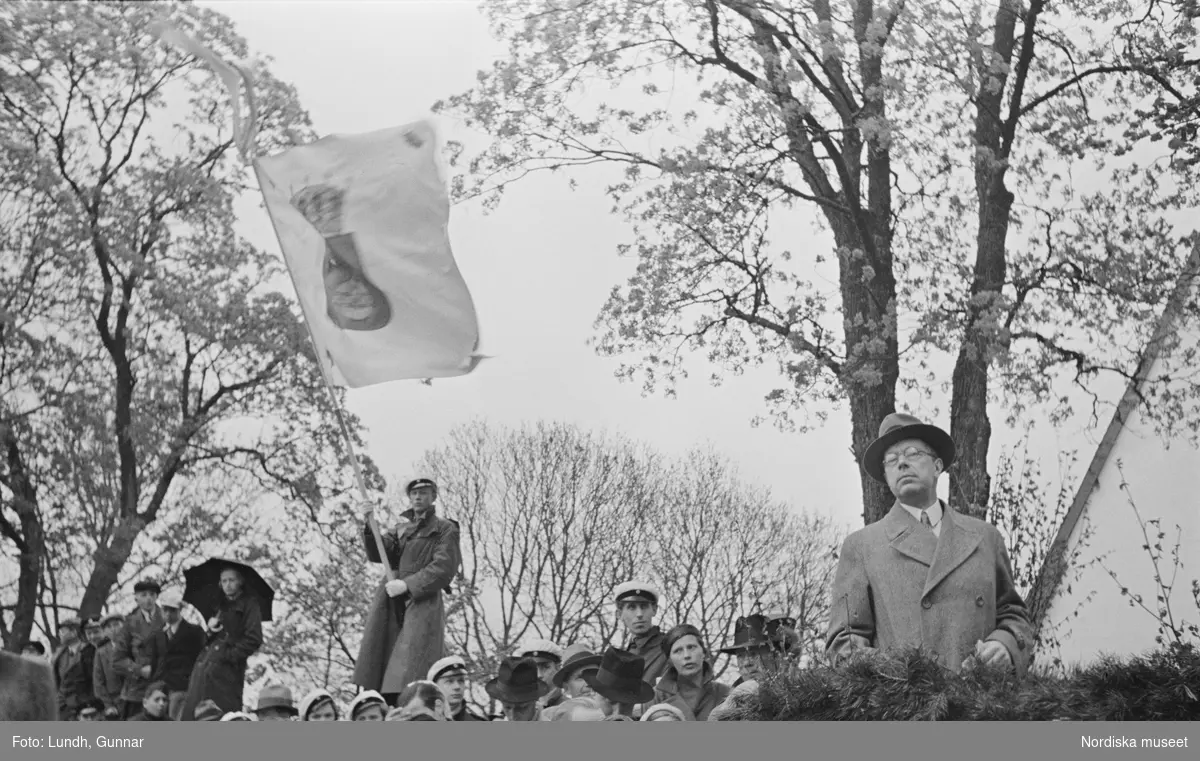 Folksamling vid hembygdsfest i Härkeberga. I bakgrunden håller en ung man i rock och studentmössa en uppländsk landskapsflagga. Längst t h kronprins Gustaf Adolf.