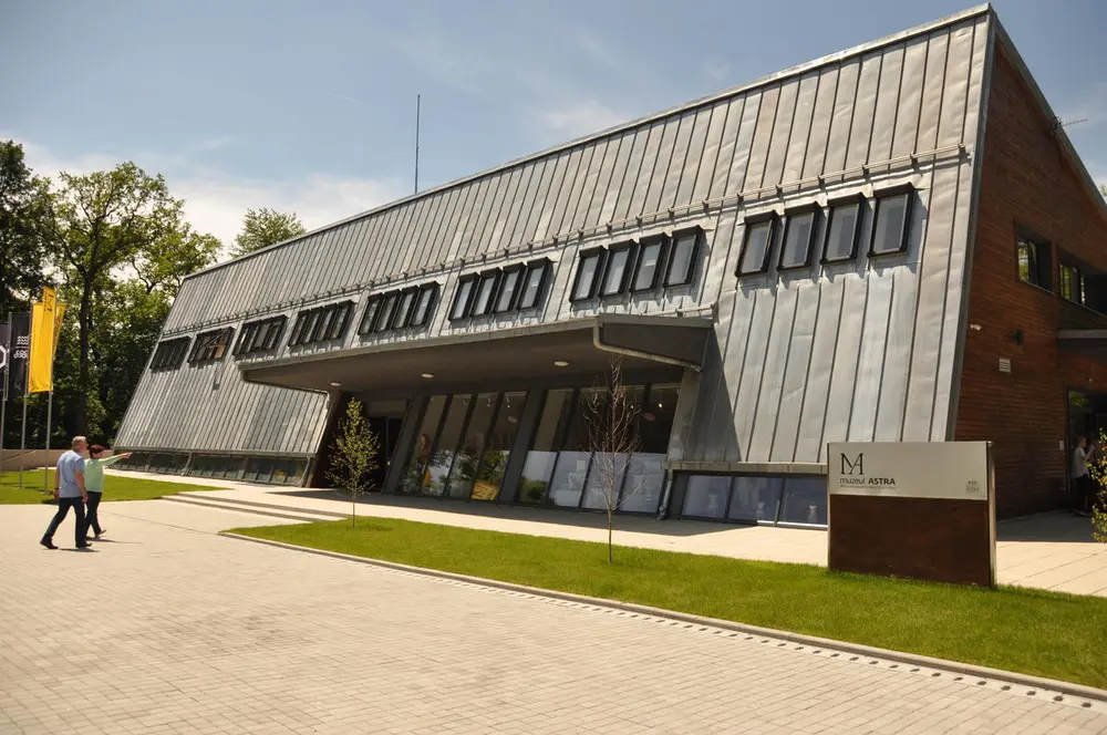Foto av mørkt stor bygning på en stor plass. Et skilt med "Museum Astra" utenfor. 
