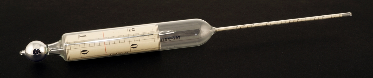 Termometer av glass  som ligger i et rundt etui av formentlig papp.