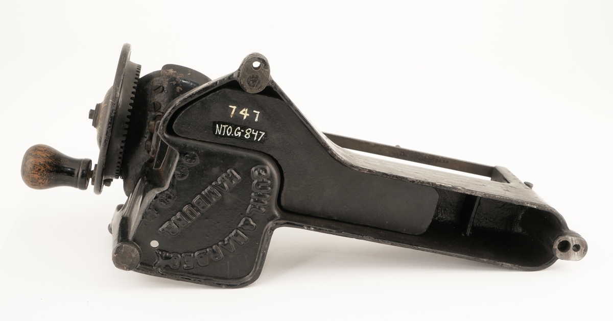 Blyantspissemaskin  av metall, sortlakkert med påskrift i gullfarge. Dreiet trehåndtak.