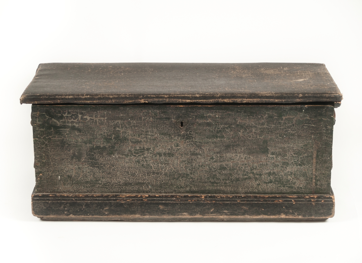 Sjömanskista, segelfartyg målat på insidan av locket.
Svartmålad och svart oljeduk ovanpå locket. Inuti finns en läddika t.h. samt ett öppet fack t.v. På lockets insida finns en fullriggare målad, den har seglen uppe och går från vänster till höger.