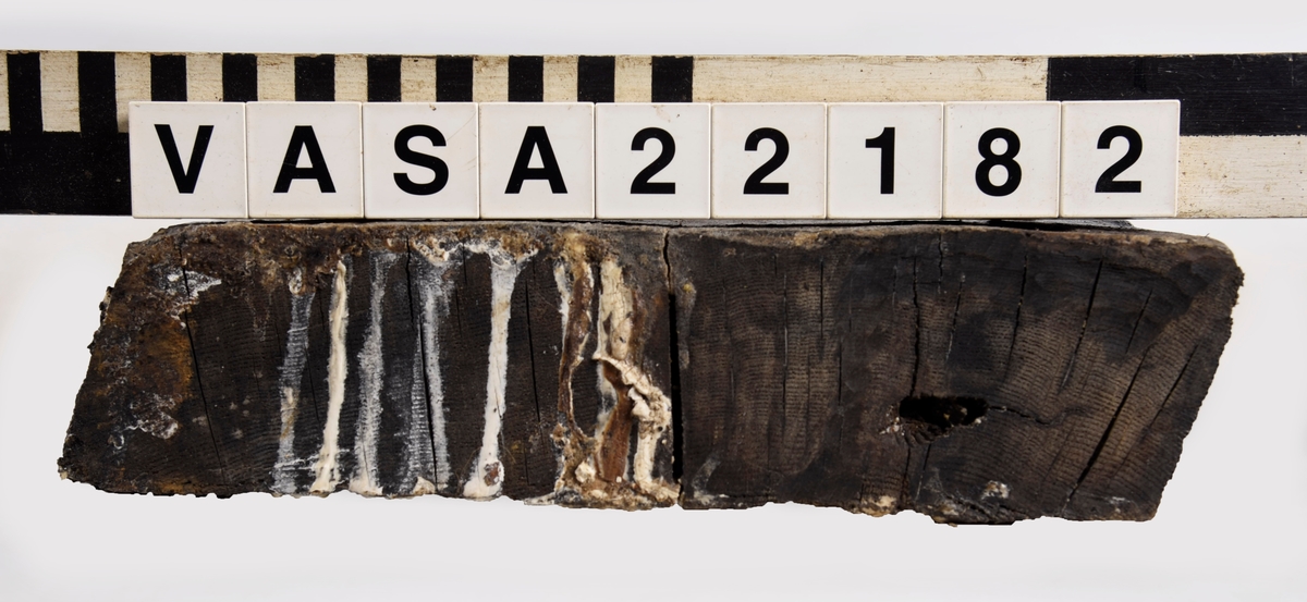 Tröskel till kanonport 14. Nästan rektangular med fasad kanter och ändar. 6 moderna skruvhål, ett klart original spikhål och ett till möjligt.
Lite deformerad, mycket vittrad på ytor (ändar bättre bevarad).