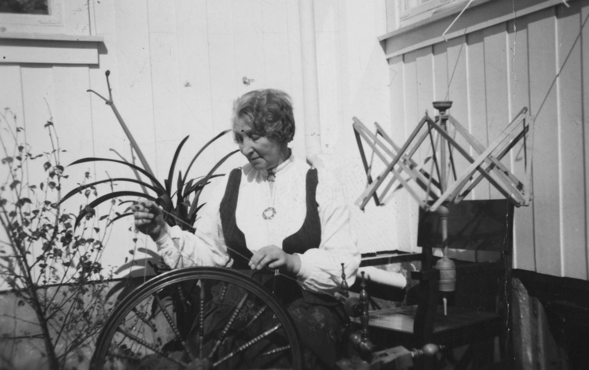 Ingelsrud, gnr.83/1. Anna Hermansen, spinner, rokk, Hedmarksbunad, garnvinne. Potteplante, mønjelilje.