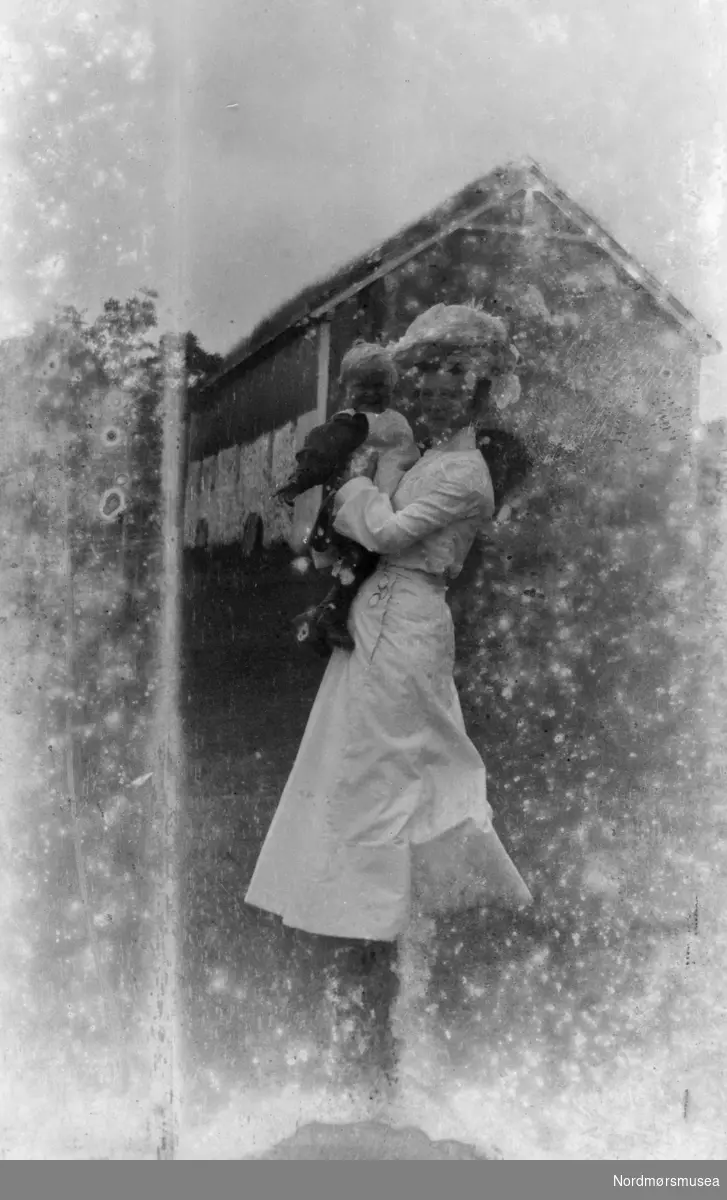 Foto av en kvinne med et lite barn. Muligens fotografert på Eidsvåg i Nesset kommune, med Georg Sverdrup som mulig fotograf. Fra Sverdrupsamlingen ved Nordmøre museums fotosamlinger.