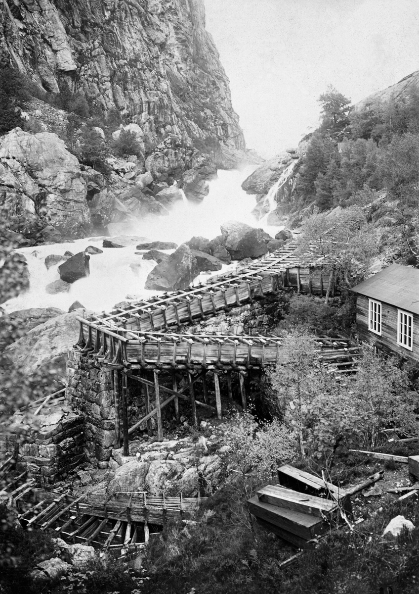 Stor laksetrapp av tre i Rjukanfossen i Siravassdraget (Sireåna) i Sokndal kommune i Rogaland. Fotografiet, som er tatt i 1908, viser Logsfossen i  motstrøms retning Sireåna. På dette stedet ble det - via et lokalt aksjeselskap, som fikk litt offentlig støtte - investert stort i fiskekultur i 1870- og 80-åra. Det ble bygd fisketrapper som skulle gjøre det mulig for laksen å gå opp Logsfossen og den ovenforliggende Rjukanfossen til Lundevatnet, og videre i dette vatnets tilløpselver. Selskapet fikk også bygd et fiskeklekkeri, som skulle sikre en stor laksdebestand i dette vassdraget. Klekkeriet kan ha vært i bygningen vi skimter en del av til høyre i dette bildet.

Innstillinga fra Stortingets næringskomité, som behandlet denne saken i budsjettåret 1883-84, er gjengitt under fanen «Opplysninger».