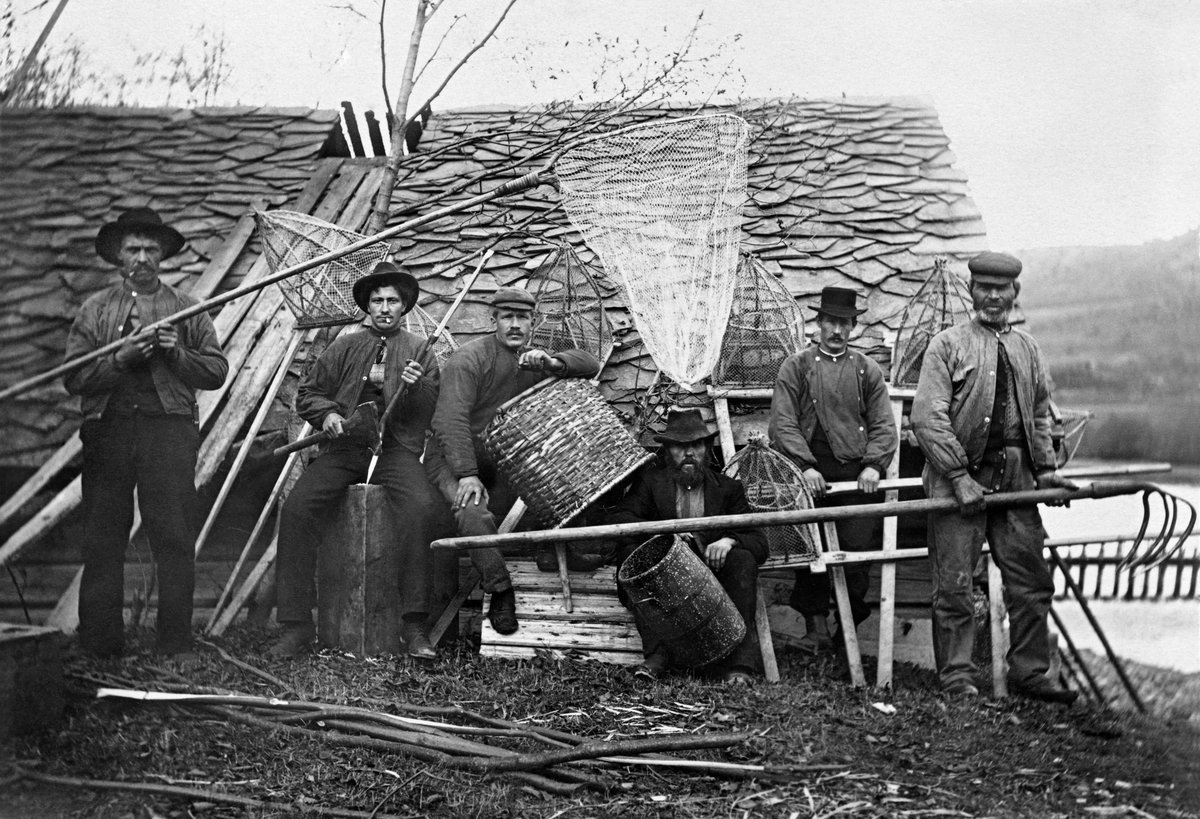 Bildet viser fiskere med forskjellig utstyr utenfor Knuvelbua i 1904.  Bildet er fra Knuvelen (Kringelen) i Fåberg (i nyere tid Lillehammer kommune). Knuvelbu. Knøvelbu. Knøvelbua. Knuvelbua. Gudbrandsdalslågen.

Tore Johan Brevik opplyste i en e-post til museet 22. oktober 2015 at mannen helt til høyre på fotografiet er hans oldefar på morssida, Hans Olson Vold, og at mannen bak ham (nest ytterst til høyre) er bestefaren, Syver Kristiansen Solbakken.

Fiskere, fiskeutstyr, fiskebu, lagesildsfiske, lågåsildfiske, fiske etter lågåsild. 

Knuvelbua ble flyttet til friluftsmuseet på Maihaugen i 1921.  Museumsgründeren Anders Sandvigs omtale av bygningen er gjengitt under fanen «Opplysninger».