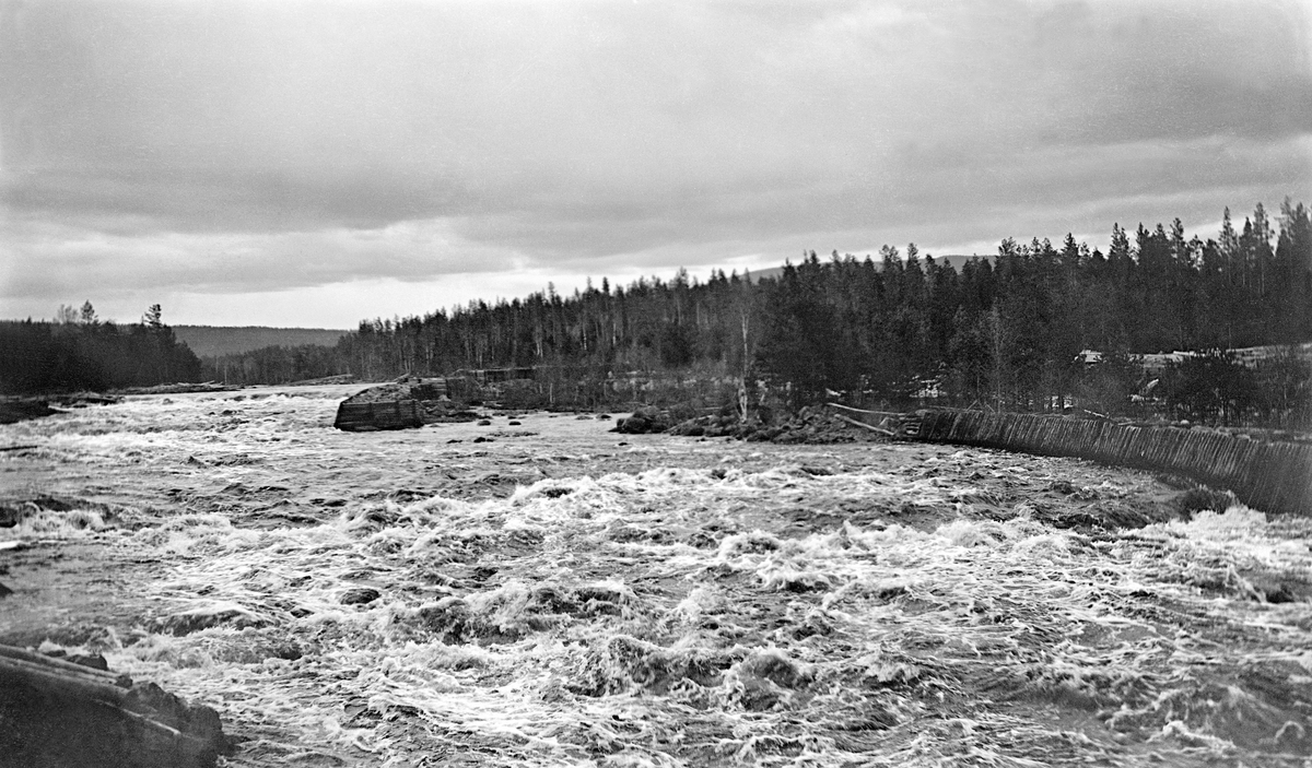 Fossestryk i elva Flisa i Åsnes i Solør.  Dette er den såkalte Valbyfossen, som har et fall på om lag 6,5 meter over en strekning på om lag 200 meter.  Fotografiet er tatt i motstrøms retning.  De kvite skumtoppene i det forholdsvis brede elveløpet indikerer at har strømmet vannet over blokkrik mark, der fløtingstømmeret lett kunne sette seg fast.  Til høyre i bilde kan det synes som om det var oppsatt en treskjerm, en såkalt "skådam", som skulle forebygge at tømmeret ble presset inn på land når flommen var på det høyeste. På dette stedet renner Flisa gjennom et forholdsvis flatt, skogdekt landskap.