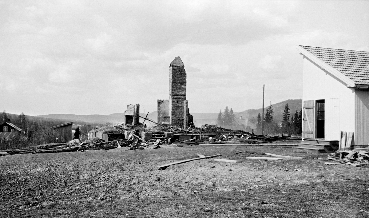 Branntomta etter «Norstua» - Christiania Tømmerdirektions da nyoppførte inspektørbolig på et høgdedrag på stasjonssida i Kongsvinger.  Brannen skal ha brutt ut 26. april 1921.  Dette fotografiet er tatt påfølgende dag.  Da sto bare de ildfaste delene av bygningskonstruksjonen - grunnmuren, pipa med tilhørende brannmurer og noe som kan se ut til å ha vært en peis - igjen.  En del forkolet treverk lå fortsatt på branntomta.  Uthusbygningen - en bordkledd bindingsverkskonstruksjon med pulttak (til høyre i bildet), ser ut til å ha kommet uskadd fra brannen. Ingeniør Egil Kopperud (1888-1970) og kona Fanny (f. 1895) hadde flyttet inn en måned før dette skjedde. Han var fløtingsinspektør i Tømmerdirektionen fra 1912. Ingeniøren var bortreist da brannen oppsto, kona var arbeidet i hagen og hushjelp Hilda Holth (1883-1959) hadde fått fri. Det var en nabo som oppdaget at det brant. Han fikk varslet fru Kopperud, og alarmert det kommunale brannvesenet. De rykket ut og tok seg inn i den brennende bygningen i håp om å kunne redde verdier. Der møtte de tjukk og kvelende røyk, men en av brannmennene greide å krabbe bort til sølvtøyskapet og berge noen verdier derfra. Snart veltet det flammer ut av hele bygningen, fra kjeller til loft. Det var 500 meter til nærmeste brannkum, så det tok tid å få rullet ut slanger, og vanntrykket var dårlig. Brannvesenet var sjanseløse i møtet med ilden – varmeutviklinga var så kraftig at de kom ikke nært nok inntil med de spede vannstrålene de hadde å hjelpe seg med. I erkjennelse av at inspektørboligen var tapt konsentrerte de seg om å spyle uthuset og telefonstolpene med vann, for å forebygge spredning av ilden. I løpet av en times tid hadde ilden fortært det meste. Bare rester av to piper raget opp på branntomta. Hvordan brannen hadde oppstått var et mysterium. Fru Kopperud benektet å ha fyrt på denne milde vårdagen, og elektrisk lys var enda ikke innlagt i huset. Observasjoner i en tidlig fase kunne tyde på at varmen kom fra badet eller fra soverommet i 2. etasje. Vinger-lensmann Rolf Johnsen (1885-1940) hadde en hypotese om at et par vannkarafler som sto i soveromsvinduet kunne ha samlet solstråler og fungert som brennglass. Bygningen var forsikret i selskapet «Norden» for 85 000 kroner og innboet var verdsatt til 40 000 kroner, store beløp med tanke på pengeverdien i 1921. Egil og Fanny Kopperud emigrerte til USA i 1923, fra 1930 bodde de i Canada. Egil Kopperud kom tilbake til Norge i midten av 1950-åra, og bodde fra da av på Smedstad i Oslo.