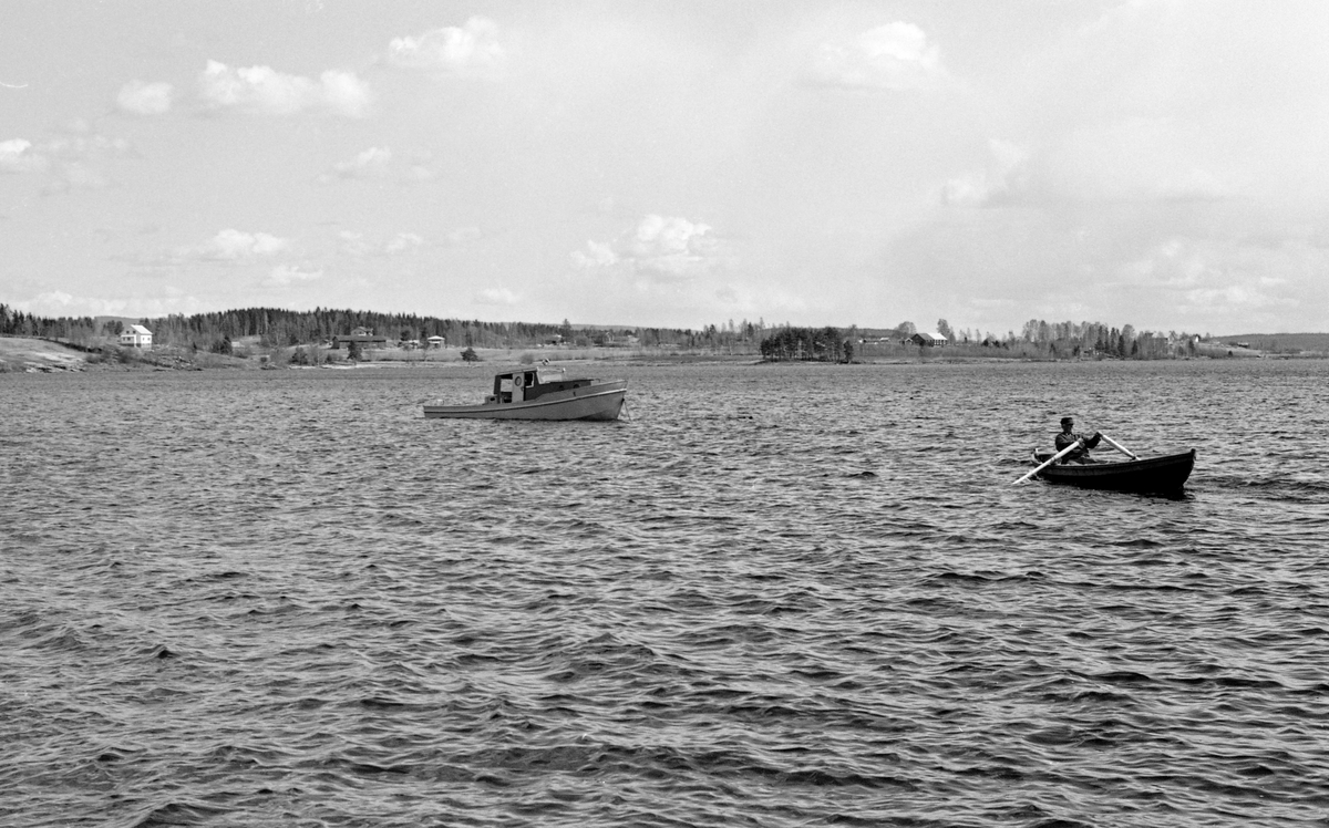 Varpebåt av stål på Storsjøen i Odalen i Hedmark våren 1958.  Fotografiet viser en mann som var i ferd med å ro ut mot den oppankrete varpebåten i en klinkbygd robåt.  I bakgrunnen skimter vi bolighus og gardsbruk langs sjøens strender.  Vannspeilet på Storsjøen har et flateinnhold på 46-47 kvadratkilometer.  Den er 16 kilometer lang og opptil 7,5 kilometer bred, og har flere sidearmer, små fjorder.  Det året da dette fotografiet ble tatt ble det meldt inn 220 889 tømmerstokker til fløting på Odalsvassdraget.