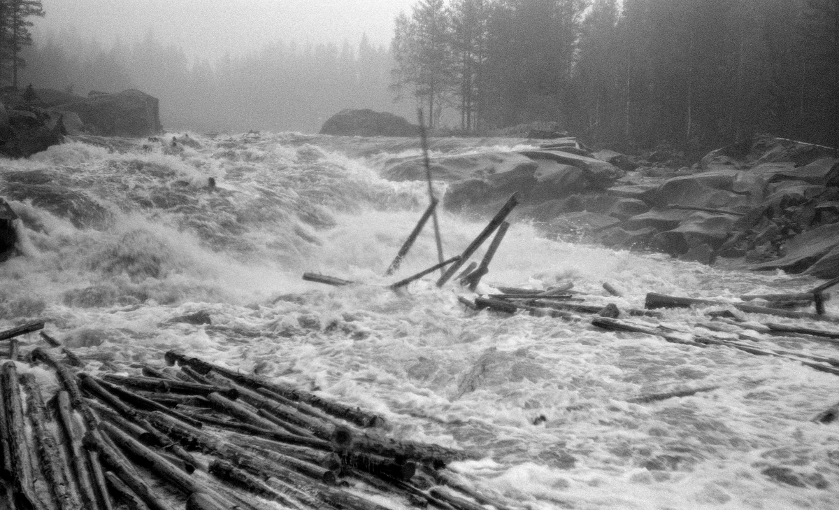 Fløting i ei flomstor elv – Flisa i Åsnes i Solør i Hedmark – våren 1960.  Bildet er fra Øvre Flisfallet, der en del tømmerstokker kom flytende i strømkavet.  Enkelte av dem reiste seg i fossen.  I forgrunnen til venstre var en del tømmerstokker drevet mot land.  Det øvre Flisfallet har et fall på 4,6 meter over en strekning på om lag 65 meter.  Dette var en lokalitet der tømmerfløterne ofte opplevde at tømmeret bandt seg i vaser, som det var både vanskelig og farlig å løsne.  Også nedenfor dette fallet gikk elva i stryk med en del oppstikkende steiner, før det nådde Ytre Flisfall, som er 165 meter langt og har et fall på 6-7 meter.