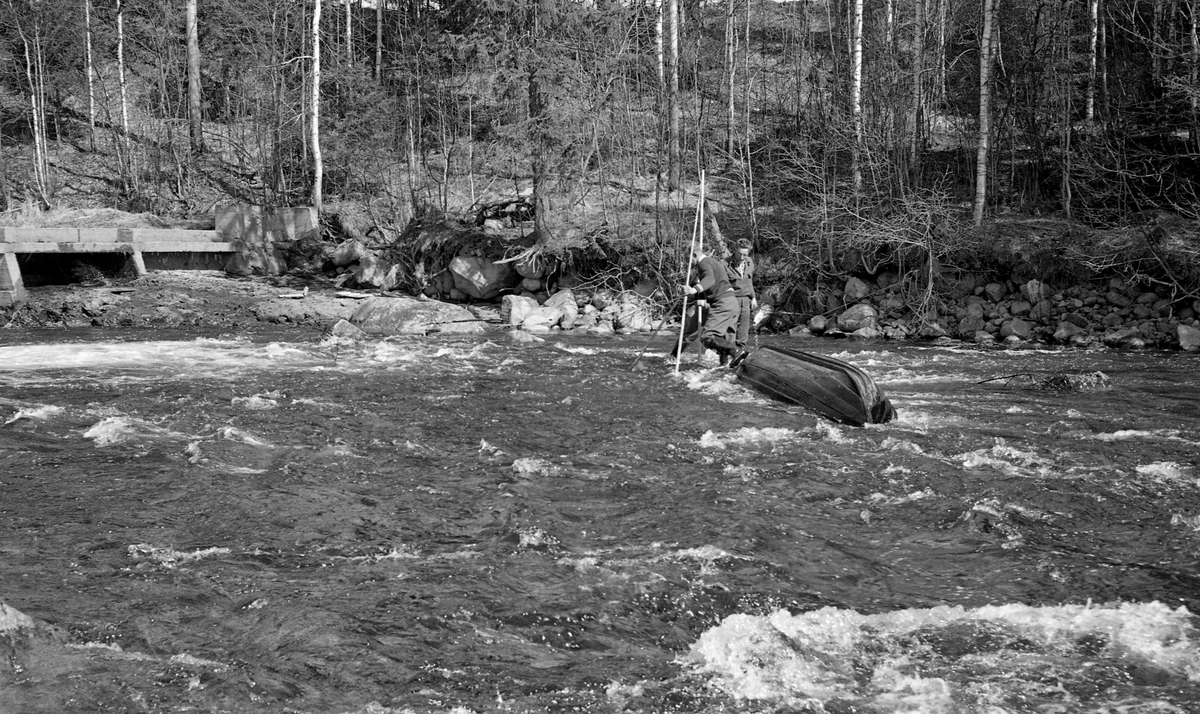 Sluttrensk i Nitelva på Nedre Romerike våren 1960.  Bildet viser to tømmerfløtere som sto på grunt vann i elva, bak en robåt som lå med kjølen i været.  Til venstre i bildet ser vi deler av betongdam.  Nitelva kommer fra Harestuevatnet i Lunner på Hadeland og går under vekslende navn sørøstover gjennom Hakadal og Nittedal mot Lillestrøm og sammenløpet med Glomma ved Fetsund.