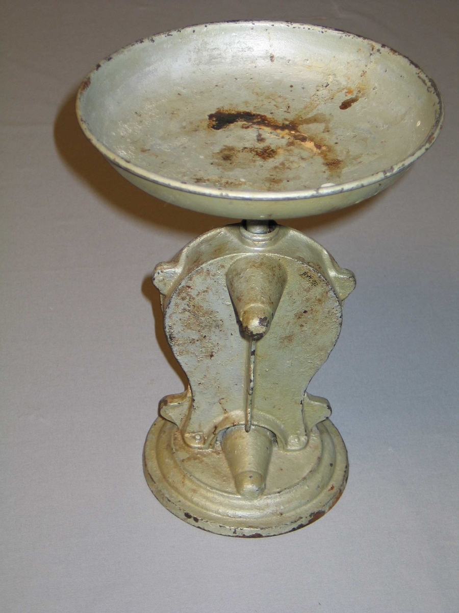 Rund fotplate, metall. Klokkeforma talskive med vektskala i gram og kilo, med visar. Sjølve talskiva av messing. Skål på toppen. Grågrøn måling.