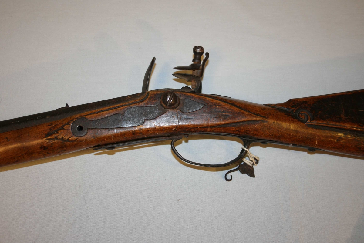 Flintlåsgevær med glatt pipe. Kolben dekorert med treskurd. 