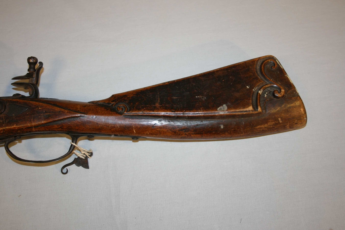 Flintlåsgevær med glatt pipe. Kolben dekorert med treskurd. 